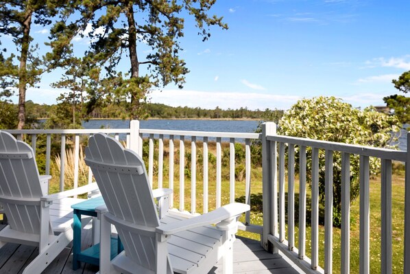 A deck with white Adirondack chairs and a small table, overlooking a lake with a white railing and trees in the background. - My Pointe of View - Spectacular Pet Friendly Waterfront with Views! (Merritt)