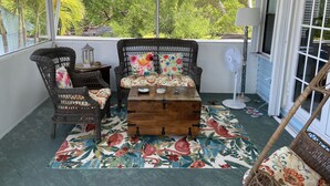 A covered balcony with wicker furniture, a wooden coffee table, and a fan.