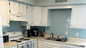 Et køkken med hvide skabe, en komfur, en opvaskemaskine og et backsplash med blå fliser.