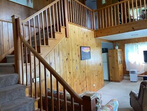 Cozy living area with a staircase leading to an upper level, featuring a large window and a kitchen area.