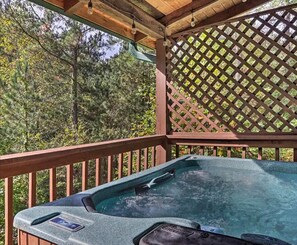 A hot tub in a wooden deck with a lattice backdrop, surrounded by trees. - Fun & Relaxation: Views, Private Hot Tub, Resort Amenities, & More!  (Pigeon Forge)