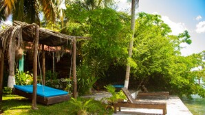 A wooden deck with a blue mat and a wooden bench, surrounded by lush greenery and palm trees. - Propiedad a Orilla de Laguna (Huay-Pix)