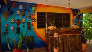 A room with a colorful mural, a wooden reception desk, and various masks on the wall. - Propiedad a Orilla de Laguna (Huay-Pix)
