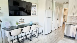 Eine moderne Küche mit Essbereich, weißen Schränken, einem großen Kühlschrank und einem flachbildfernseher, der über der Arbeitsplatte angebracht ist.