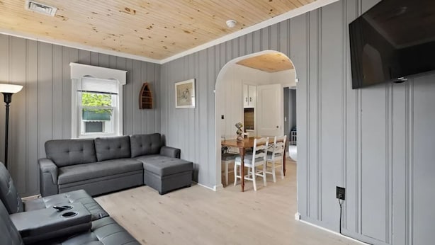 Un salon moderne avec un canapé d’angle, un coin repas comprenant une table et des chaises en bois, et un téléviseur fixé au mur.