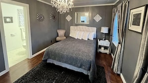 A bedroom with a large bed, a chandelier, a bedside table with a lamp, and a mirror on the wall. - Cascade Motel (Cascade Locks)