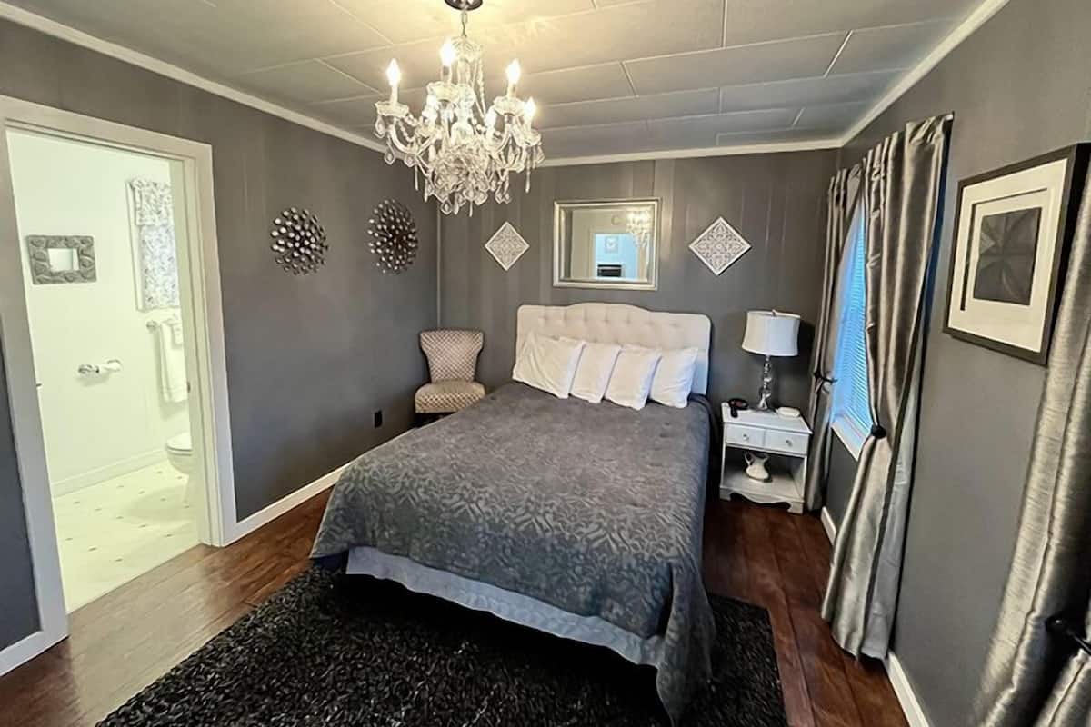 Un dormitorio con una cama grande, un candelabro, una mesita de noche con lámpara y un espejo en la pared.