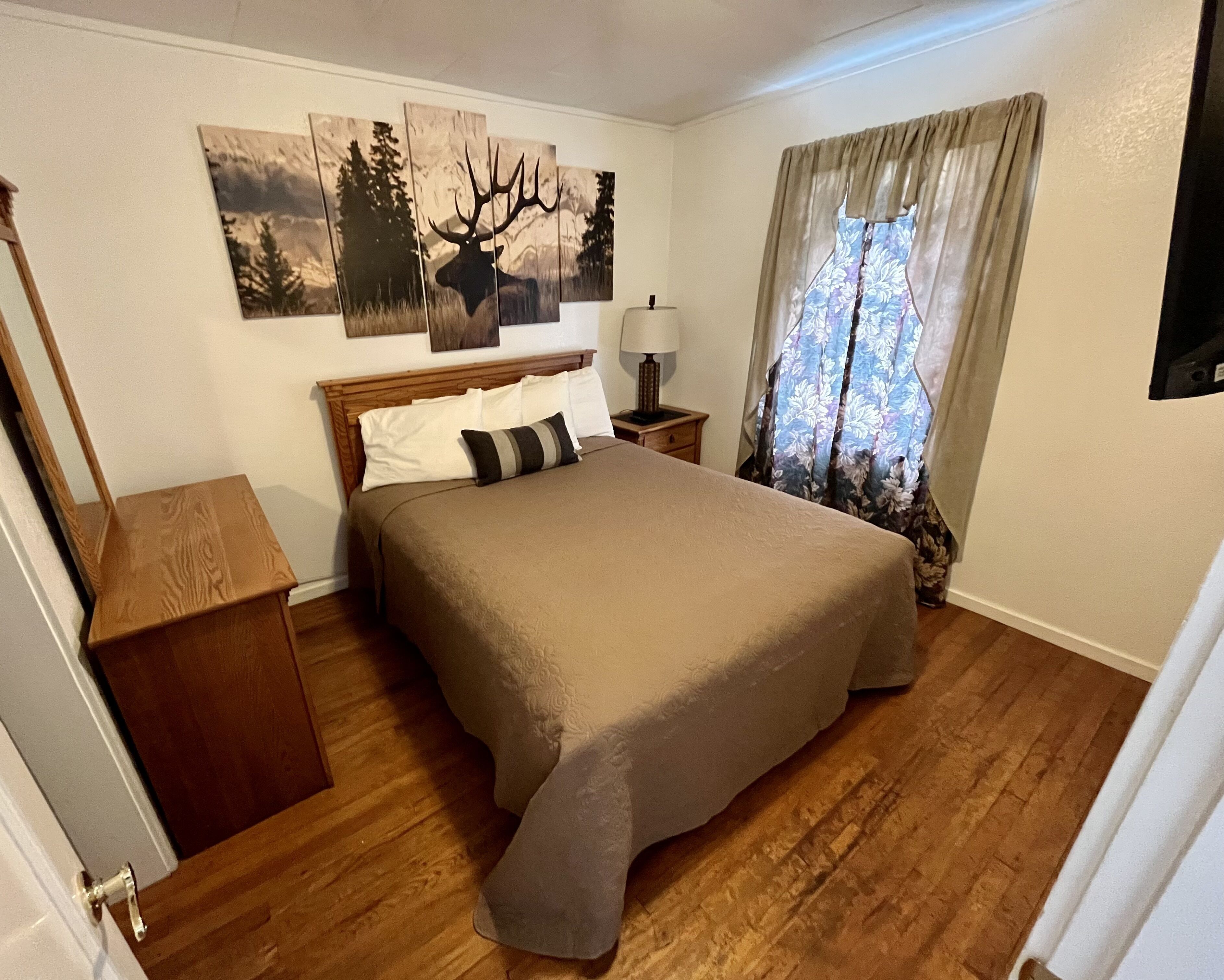 Une chambre à coucher avec un lit en bois, une table de chevet, une lampe et une fenêtre avec des rideaux.
