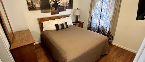 A bedroom with a wooden bed, a nightstand, a lamp, and a window with curtains.