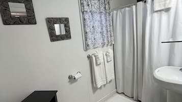 Een badkamer met toilet, wastafel, douchegordijn, handdoeken en een klein kastje.