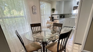 A dining area with a glass table and chairs, a kitchen in the background, and a patterned rug on the floor. - Cascade Motel (Cascade Locks)