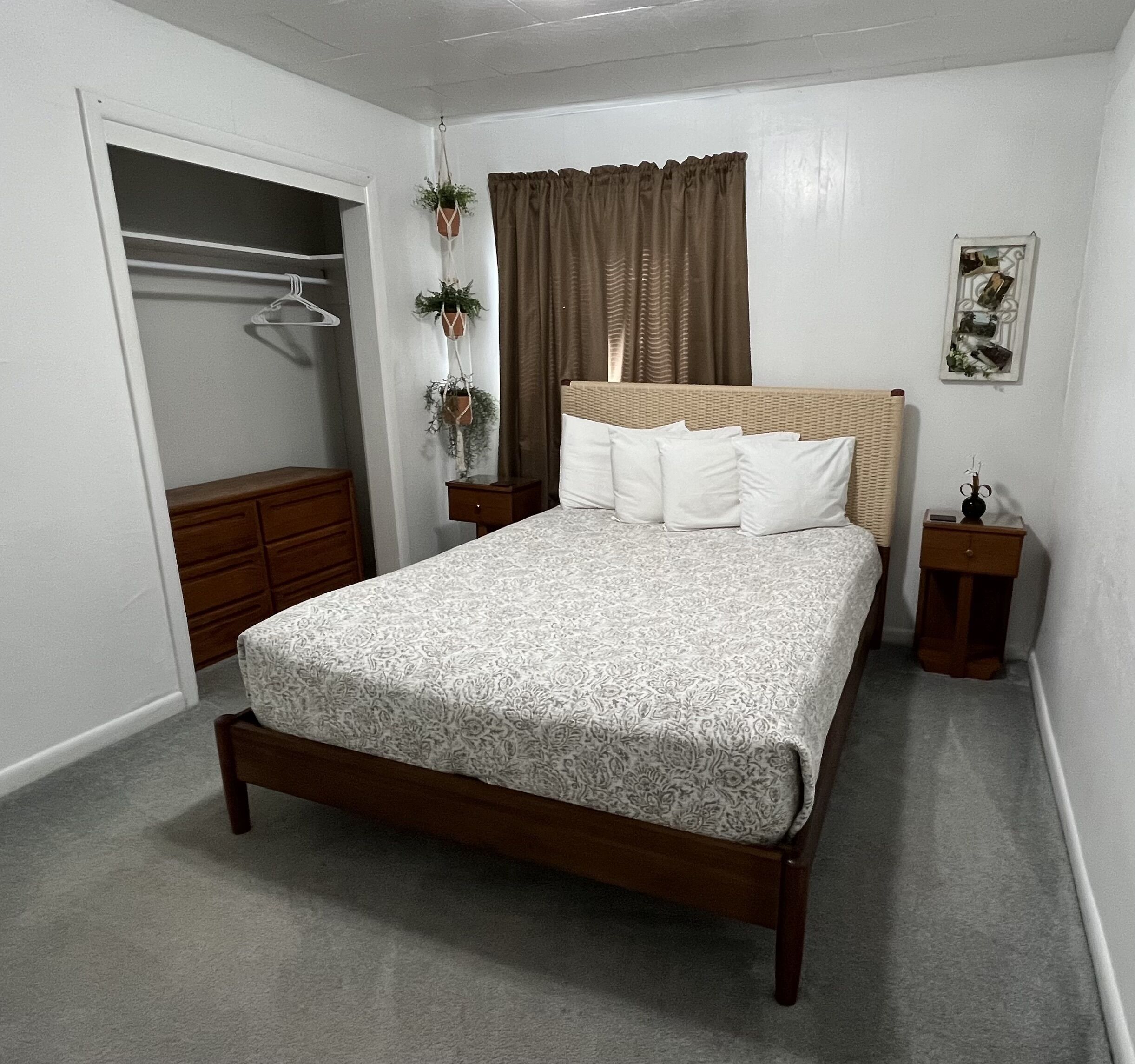A bedroom with a bed, a wardrobe, a bedside table, and a hanging plant.