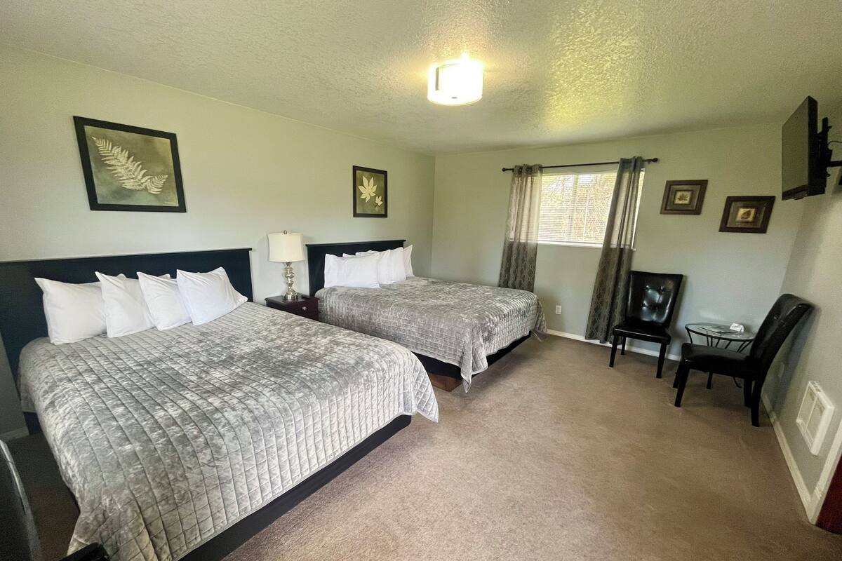 Habitación de hotel con dos camas, un escritorio, una silla y un ventanal con cortinas.