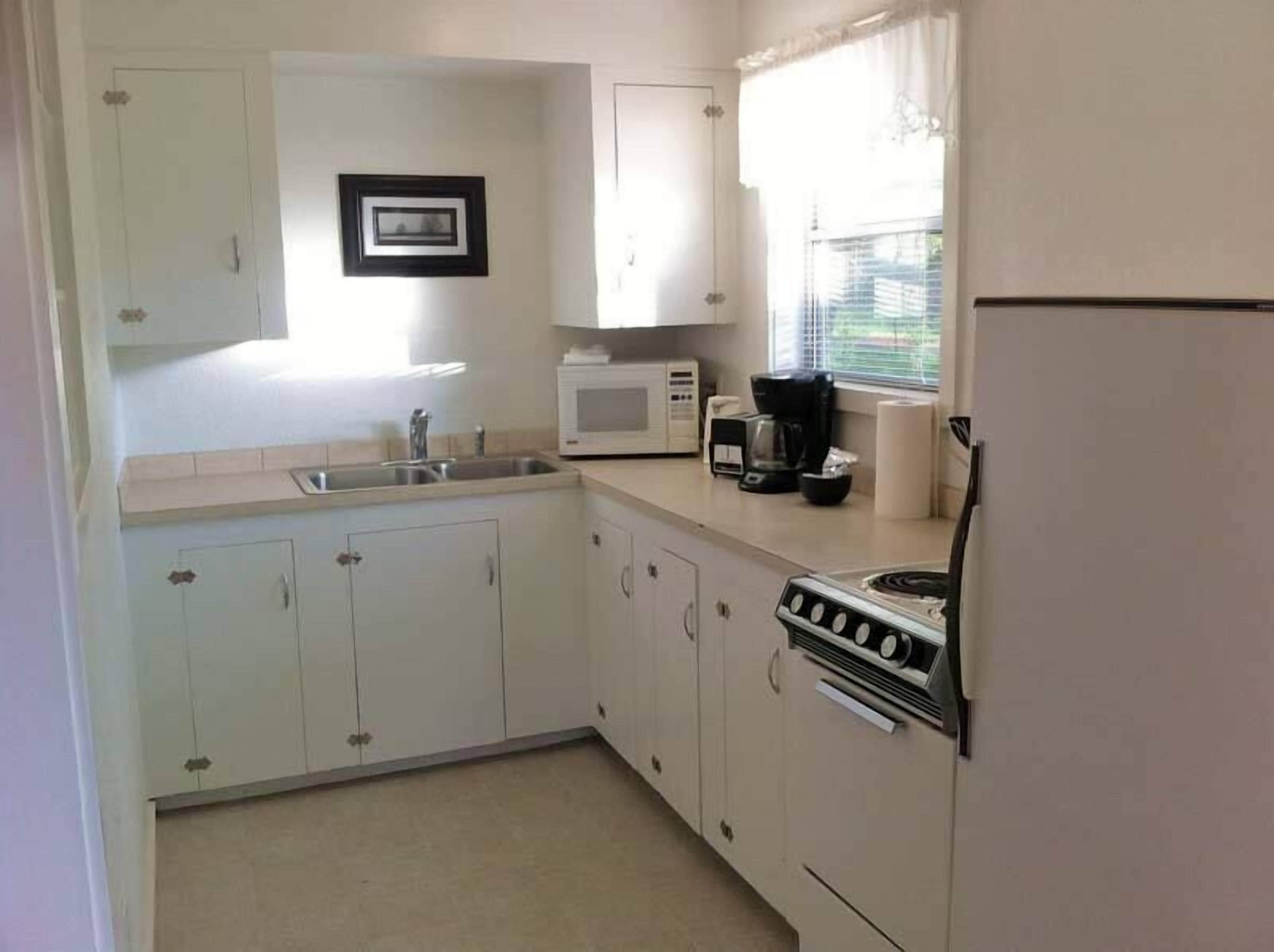 A compact kitchen with white cabinets, a sink, a microwave, a coffee maker, and a stove.