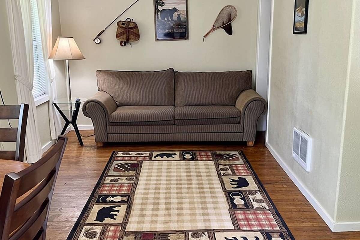 Un salón con un sofá marrón, un tapete estampado y decoraciones en la pared, incluyendo un oso y un pez.
