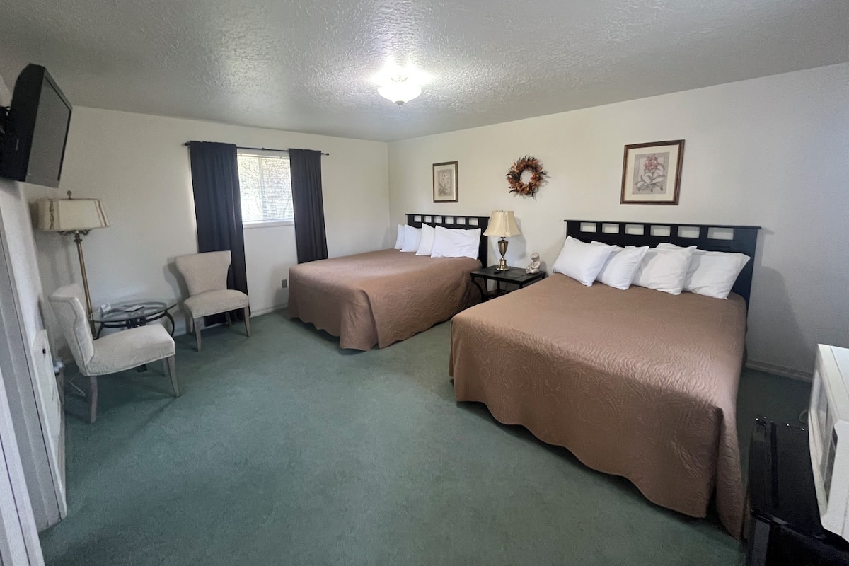 Habitación de hotel con dos camas, una silla, una mesita, un televisor y una ventana con cortinas.