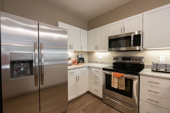 A modern kitchen with stainless steel appliances, white cabinets, and a granite countertop.