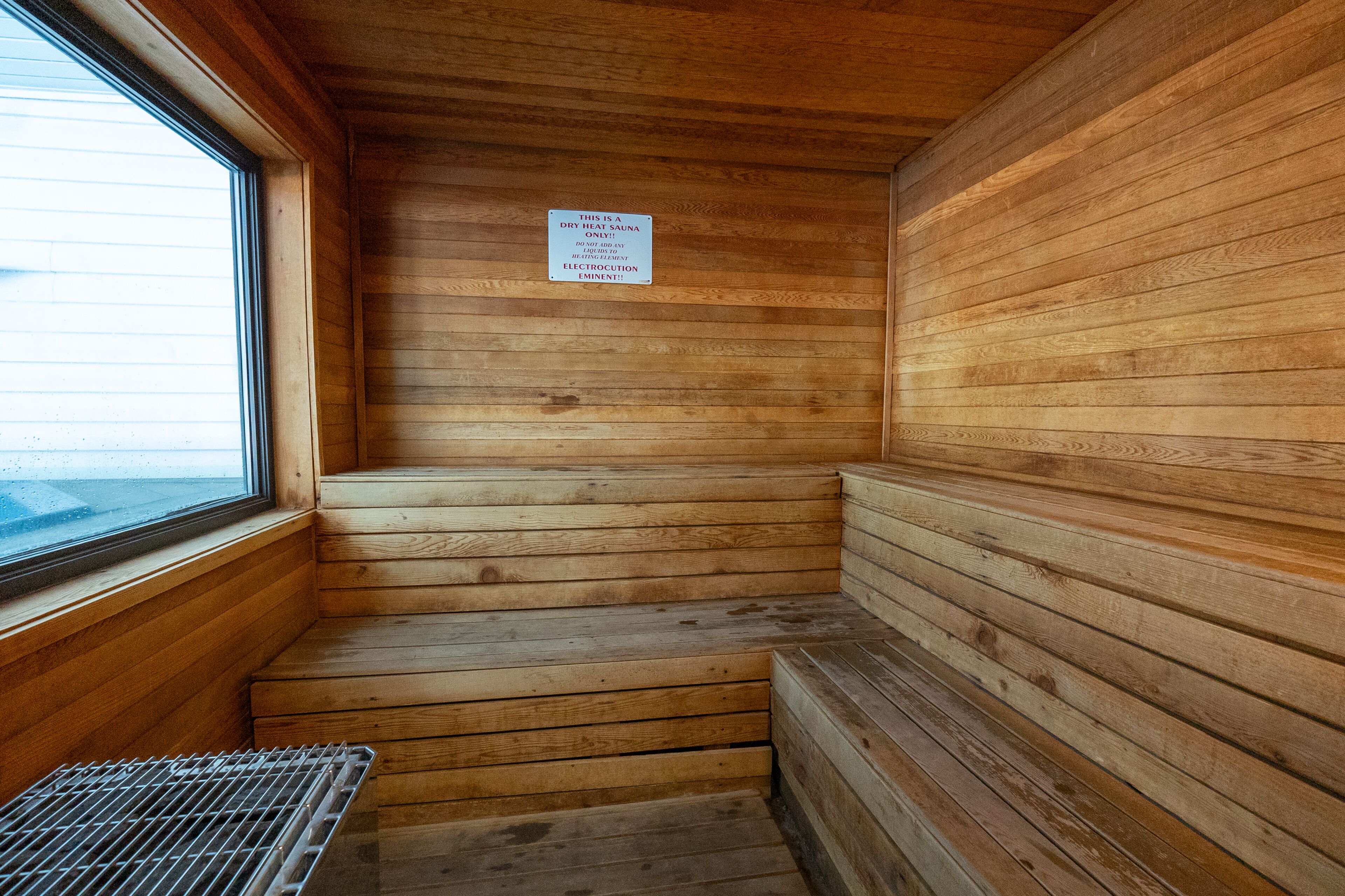 A sauna with wooden walls and benches, a window, and a sign indicating it is a dry sauna.
