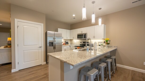 A modern kitchen with white cabinets, stainless steel appliances, and a granite island with bar stools. - New Build Walk-In 3BR Branson Condo w/ Indoor Pool | (FH-G203) (Branson)