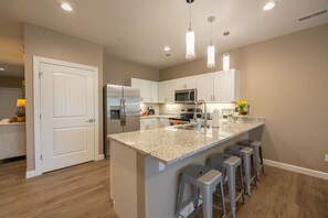 A modern kitchen with white cabinets, stainless steel appliances, and a granite island with bar stools.