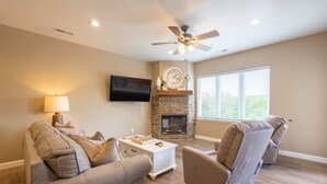 A living room with a fireplace, a ceiling fan, and a television mounted on the wall. - New Build Walk-In 3BR Branson Condo w/ Indoor Pool | (FH-G203) (Branson)