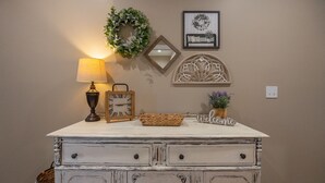 A white dresser with drawers, a lamp, a clock, a mirror, a welcome sign, and a decorative wall piece. - New Build Walk-In 3BR Branson Condo w/ Indoor Pool | (FH-G203) (Branson)