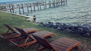 A waterfront area with wooden lounge chairs and a wooden pier extending into the water.