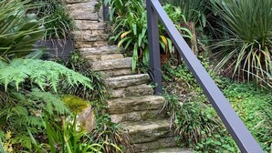 Eine steinerne Treppe mit Metallgeländern, umgeben von üppigem Grün und Pflanzen.