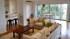 Ein modernes Wohnzimmer mit Sofa, Couchtisch und Barhocker. Es gibt einen Essbereich mit Tisch und Stühlen sowie eine Küche mit Schränken und einer Arbeitsplatte.