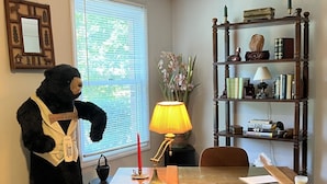 Una habitación con escritorio, lámpara, estantería y una estatua de oso.