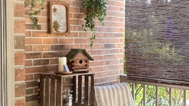 Un rincón exterior acogedor con dos sillas a rayas, una mesita y un comedero decorativo en una pared de ladrillo.