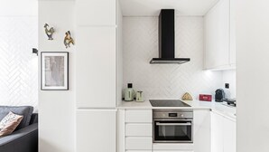 Une cuisine moderne avec des meubles blancs, une hotte noire, un four encastré et un dosseret décoré d’un motif en chevrons.