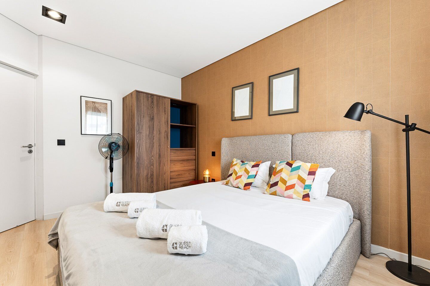 Habitación de hotel con cama, ventilador, armario y lámpara de noche.