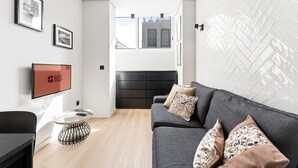 Un salon moderne avec un canapé, un téléviseur et un luminaire fixé au mur.