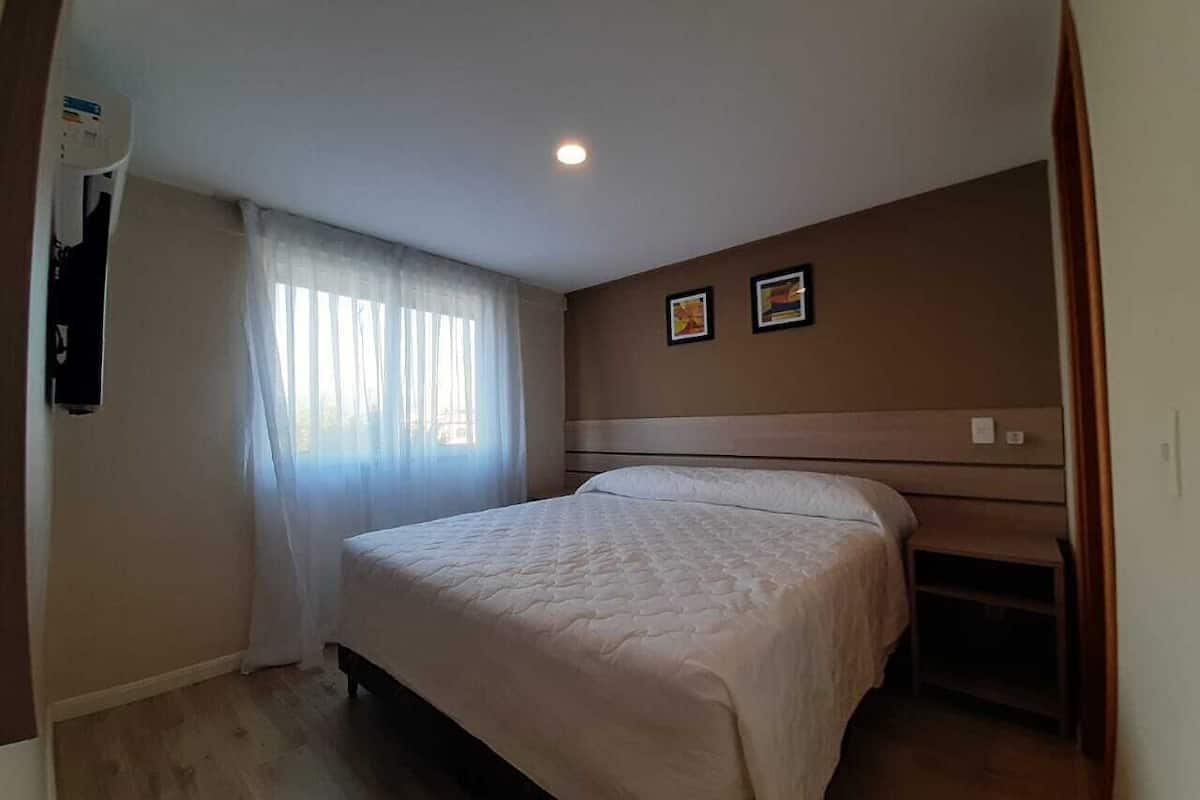 Une chambre à coucher comprenant un lit, une table de chevet, un climatiseur fixé au mur et une fenêtre avec des rideaux.