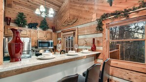 A wooden cabin kitchen with a bar area, wooden cabinets, a microwave, a stove, and a large window overlooking trees. - Secluded Mountain Getaway - Spring Sale (Sevierville)