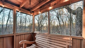 A wooden bench with a chain hanging from the ceiling, positioned in front of large windows with a view of trees and mountains. - Secluded Mountain Getaway - Spring Sale (Sevierville)