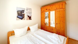 Una camera da letto con un'armadio in legno, un letto con biancheria bianca e due quadri appesi al muro.