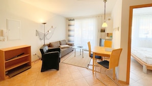 Een gezellig, compact leefruimte met een bank, een eettafel met stoelen, een klein bijzettafeltje, een televisie en een bed.
