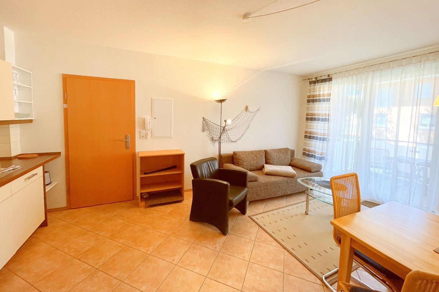 A compact living space with a kitchenette, a sofa, a dining table, and a large window with curtains.