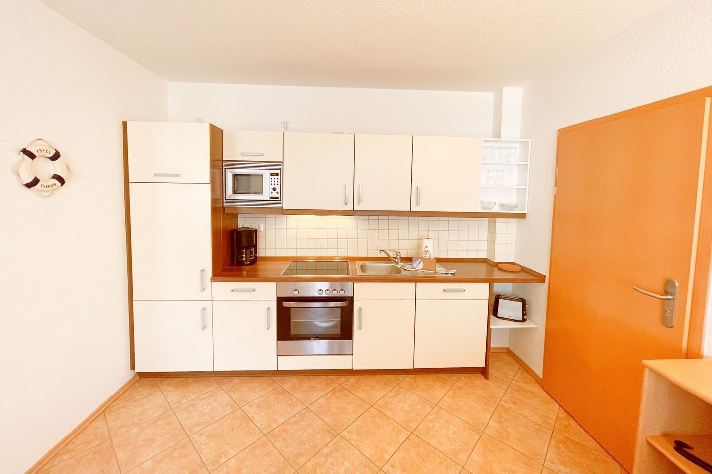 Una cocina compacta con gabinetes blancos, microondas, estufa y lavaplatos.