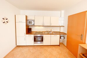 Una cocina compacta con gabinetes blancos, microondas, estufa y lavaplatos.