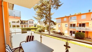 Een balkon met een tafel en stoelen, met uitzicht op een woonwijk met oranje gebouwen en een boom.