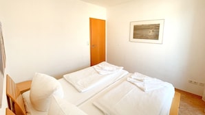 Een eenvoudige, schone kamer met twee bedden, een houten deur en een ingelijste foto aan de muur.