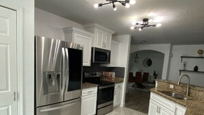 A modern kitchen with stainless steel appliances, white cabinetry, and a granite countertop. - Home Away from Home (Haines City)