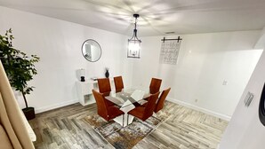 A dining area with a glass table, brown chairs, a potted plant, a white cabinet, and a hanging light fixture. - Home Away from Home (Haines City)