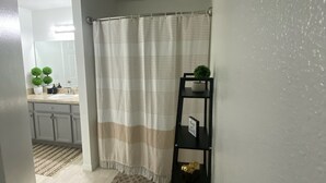 A bathroom with a striped shower curtain, a black shelf with a plant, and a light-colored floor. - Home Away from Home (Haines City)