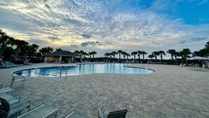 A swimming pool with a curved edge, surrounded by lounge chairs and palm trees. - Home Away from Home (Haines City)