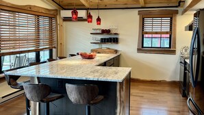 A kitchen with a wooden ceiling, a marble countertop island with stools, and a refrigerator. - BRAND NEW, WALK EVERYWHERE! Amazing Views & Luxury in the Heart of Lake Placid (Lake Placid)