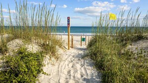 En sandstig som leder till stranden och vidare ut mot havet, med en skylt som visar var man kan komma åt stranden.